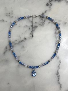 a blue beaded necklace with a tear shaped pendant hangs on a marble countertop