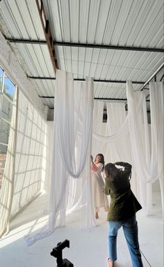 two people taking pictures in front of white curtains