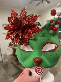 a hand holding a green mask with red and gold decorations on it's face