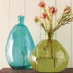 two vases with flowers in them sitting on a wooden table next to each other