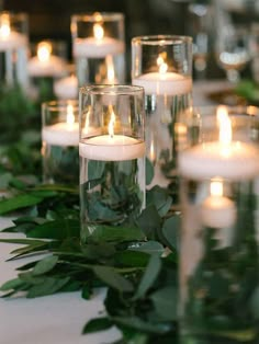 candles are lined up on a table with greenery