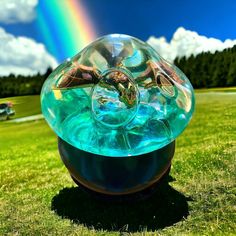 a large glass ball sitting on top of a lush green field with a rainbow in the background