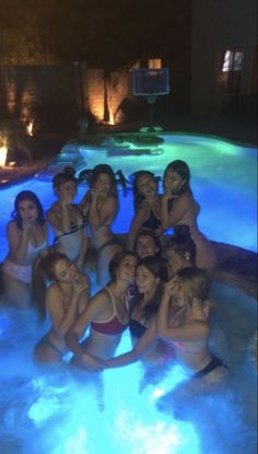 a group of young women sitting in the middle of a swimming pool at night time