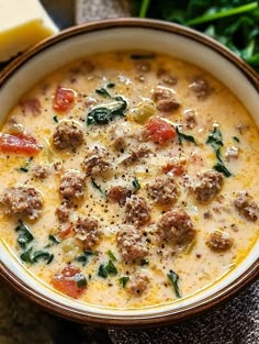 a bowl of soup with meatballs, spinach and cheese on the side next to some bread