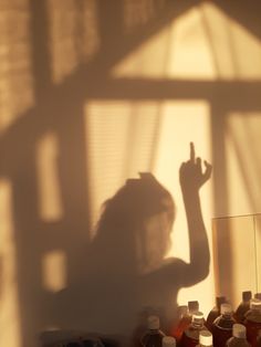 the shadow of a woman holding her hand up in front of a mirror with bottles behind it