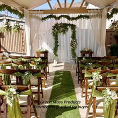 an outdoor ceremony setup with green chairs and white drapes on the ceiling, decorated with greenery