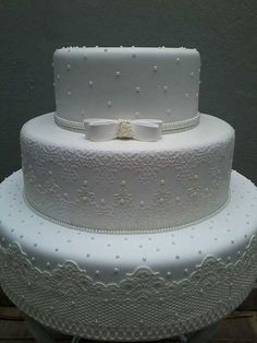 a three layer white wedding cake with pearls and bows on it's tiers