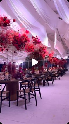 a large tent with tables and chairs covered in white draping, red flowers hanging from the ceiling