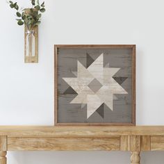 a wooden table topped with a vase filled with flowers next to a framed star quilt