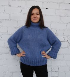 a woman standing in front of a white brick wall wearing a blue turtle neck sweater