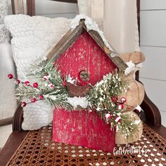 a red birdhouse decorated with greenery, berries and pine cones on a table