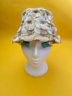 "This unique 60s hat is made from a cream floral stiffened lace with a petersham band and a wired circular brim with cream velvet edging. It is decorated with cream, peach and beige daisies with velvet and satin petals, beaded stamens, fluffy centres and lime green satin leaves. Condition Amazing condition with no damage. Measurements: Circumference of Petersham Band: 22.5\" 57cms Circumference of Wired Band: 25\" 63.5cms Crown to Brim: 5\" 13cms" Vintage Cream Fascinator For Royal Ascot, Cream Vintage Fascinator For Royal Ascot, Vintage White Hat With High Crown, Vintage White High Crown Hat, Cream Mini Hats For Vintage Events, Vintage Cloche Hat For Spring Evenings, Cream Cloche Mini Hat For Royal Ascot, White Vintage Cloche Mini Hat, Vintage White Cloche Mini Hat