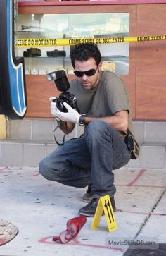 a man kneeling down with a camera in front of him and some caution tape on the ground