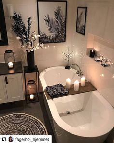 a white bath tub sitting in a bathroom next to two candles and pictures on the wall