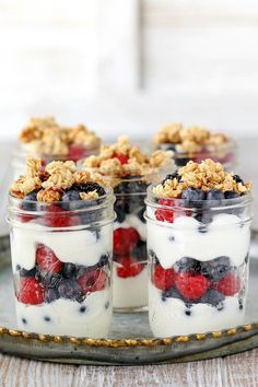 three jars filled with yogurt, berries and granola on a metal tray