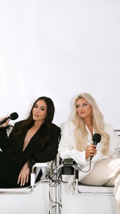 two women sitting next to each other on a white couch with microphones in front of them