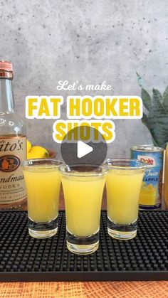 three shot glasses filled with orange juice on top of a table next to bottles of alcohol