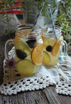 two mason jars filled with lemonade and blackberries on a doily next to a potted plant