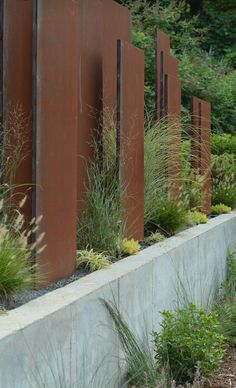 a row of metal sculptures sitting on top of a cement wall next to grass and bushes