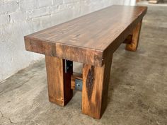 a wooden bench sitting on top of a cement floor next to a white brick wall