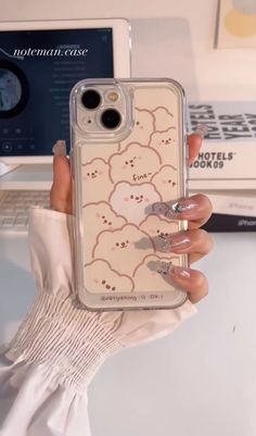 a woman holding up her phone case with clouds on the front and back, in front of a laptop