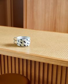 a cup sitting on top of a wooden table next to a bar stool with a black and white polka dot pattern