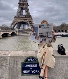 a woman sitting on a ledge reading a newspaper in front of the eiffel tower