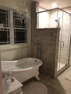 a bath tub sitting next to a window in a bathroom under a chandelier