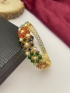 This stunning handcrafted bangle bracelet features a vibrant combination of multicolor stones and pearls set in a luxurious gold-plated design. Perfect for adding a splash of color to any outfit, this bangle is ideal for bridal jewelry or festive occasions such as weddings, Diwali, or family celebrations. The intricate detailing and adjustable fit make this bracelet both stylish and comfortable, ensuring it can be worn for any event with ease. This ethnic cuff bangle is a versatile accessory that can complement both traditional and contemporary outfits, making it a must-have for jewelry lovers. Whether you're looking for a standout piece for your bridal collection or a unique gift for someone special, this handcrafted multicolor bangle is sure to impress. Elegant Multicolor Festive Bracelets, Festive Multicolor Gemstone Bracelets, Elegant Multicolor Cuff Bracelet For Festive Occasions, Elegant Multicolor Gold Plated Bracelets, Elegant Multicolor Gold-plated Bracelets, Multicolor Cuff Bracelet For Weddings, Multicolor Multi-stone Bangle For Weddings, Multicolor Gold Plated Bracelet, Multicolor Jeweled Bangle