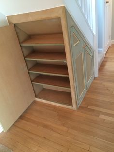 an open cabinet in the corner of a room next to a stair case and wooden floor