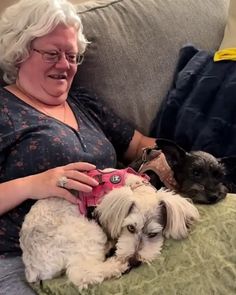 a woman sitting on a couch with two dogs in her lap and one is holding a camera