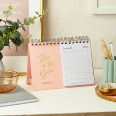 a desk with a calendar, pen and potted plant next to it on the table