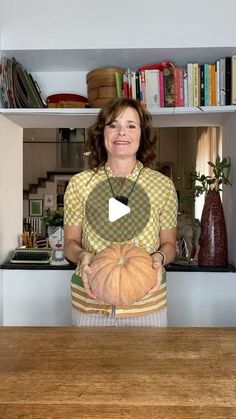 a woman holding a pumpkin in front of a book shelf with books on the shelves