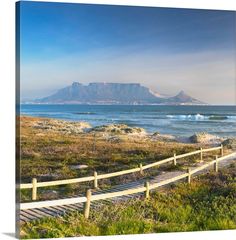 a wooden path leading to the ocean with mountains in the background and grass on either side