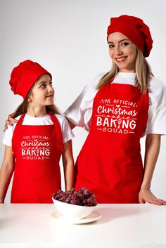 two women in red aprons standing next to a bowl of grapes