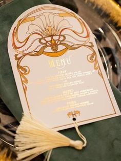 a menu is sitting on top of a green table cloth with gold trim and tassels