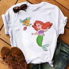 a white shirt with the little mermaid and fish on it, next to some shoes