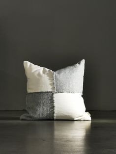 a white and grey pillow sitting on top of a wooden floor next to a gray wall