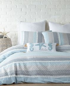 a bed with blue and white comforters in front of a brick wall next to a wicker basket