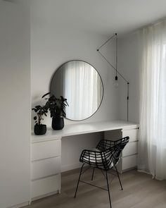 a white desk with a round mirror on the wall next to a chair and potted plant