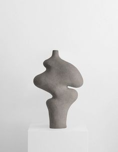 a gray sculpture sitting on top of a white pedestal in front of a white wall