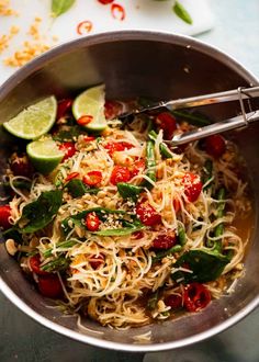 a bowl filled with noodles and vegetables on top of a blue table cloth next to sliced limes