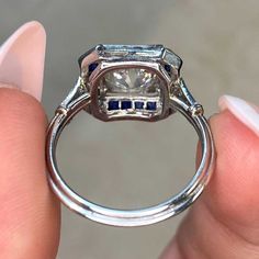 someone is holding an engagement ring with blue sapphire stones on the sides and two diamonds in the middle