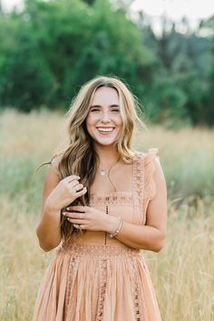 a woman standing in tall grass with her hands on her chest and smiling at the camera