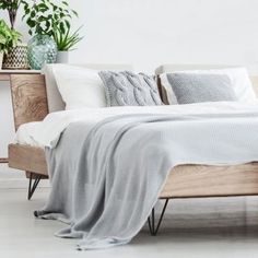 a bed with white sheets and pillows next to a potted plant on a shelf