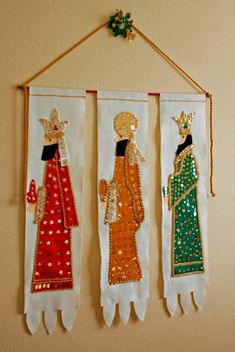 three handmade wall hangings with gold and green designs on them, each featuring an image of two women