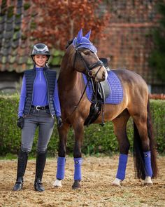 a woman standing next to a brown horse wearing a blue sweater and riding boots on