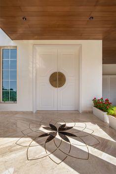 a large white door sitting next to a planter filled with red flowers on top of a hard wood floor