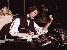 a man sitting at a desk with a book and pen in his hand while writing