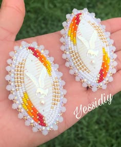 two white and yellow beaded earrings on a person's hand with grass in the background